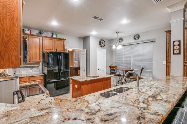 kitchen featuring a sink, brown cabinetry, freestanding refrigerator, visible vents, and a kitchen island