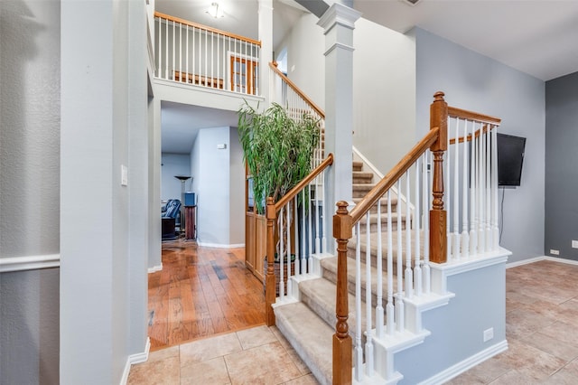 stairway with baseboards, a high ceiling, tile patterned floors, and ornate columns