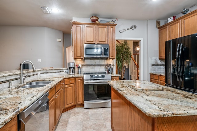 kitchen featuring a sink, brown cabinets, backsplash, light stone countertops, and appliances with stainless steel finishes