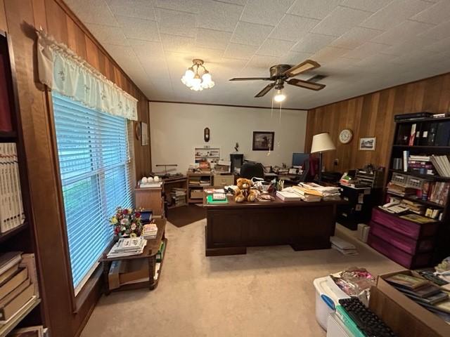 home office featuring light colored carpet, wooden walls, and ceiling fan