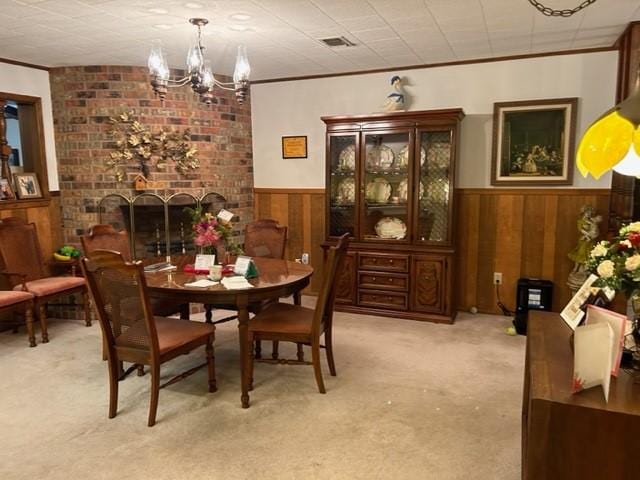 dining space with a notable chandelier, wainscoting, wood walls, crown molding, and light colored carpet