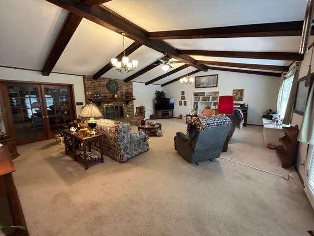 living area with carpet, lofted ceiling with beams, a brick fireplace, and a notable chandelier