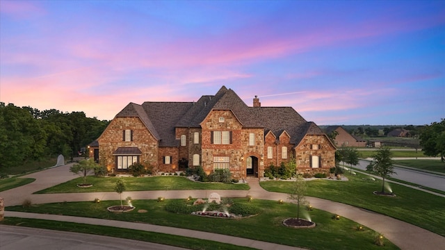 view of front of house featuring curved driveway, a chimney, stone siding, and a front yard