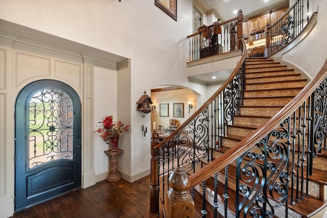 entryway featuring a towering ceiling, dark wood finished floors, crown molding, arched walkways, and baseboards