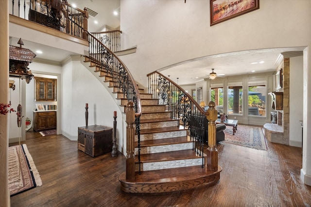 stairs featuring wood finished floors, a ceiling fan, crown molding, a towering ceiling, and arched walkways