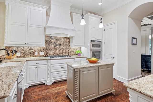 kitchen featuring a sink, premium range hood, crown molding, arched walkways, and appliances with stainless steel finishes