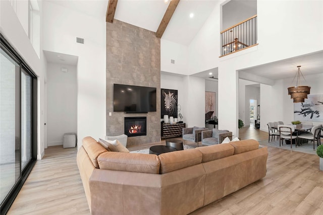living room featuring high vaulted ceiling, light wood-style flooring, a fireplace, beamed ceiling, and baseboards