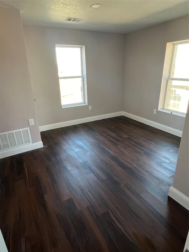 414 Ussery, Bowie, TX 76230 - spare room with baseboards, a wealth of natural light, visible vents, and dark wood-style floors