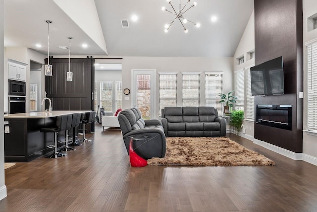 13101 Scissortail Dr, Frisco, TX 75035 - living room with high vaulted ceiling, dark wood-type flooring, a chandelier, recessed lighting, and a glass covered fireplace