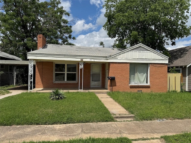 view of front of home featuring a chimney, a porch, brick siding, and a front lawn