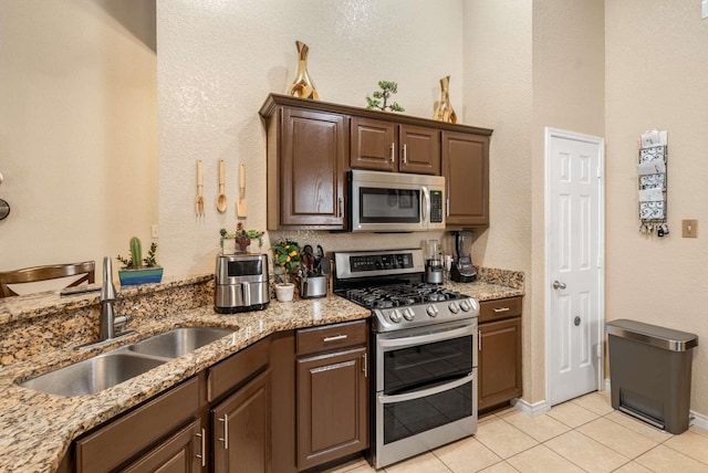 6113 Tilapia Dr, Fort Worth, TX 76179 - kitchen featuring stainless steel appliances, a sink, light tile patterned floors, light stone counters, and dark brown cabinetry