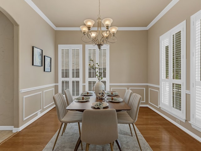 dining room featuring ornamental molding, a chandelier, wood finished floors, arched walkways, and a decorative wall