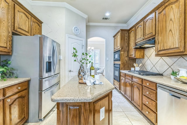 kitchen featuring black appliances, under cabinet range hood, a center island, arched walkways, and tasteful backsplash