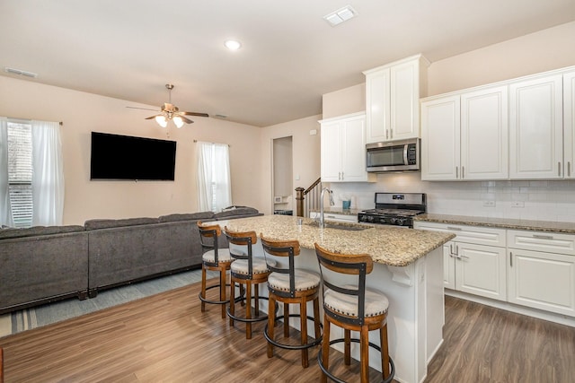 kitchen with appliances with stainless steel finishes, a sink, dark wood-style floors, a ceiling fan, and tasteful backsplash