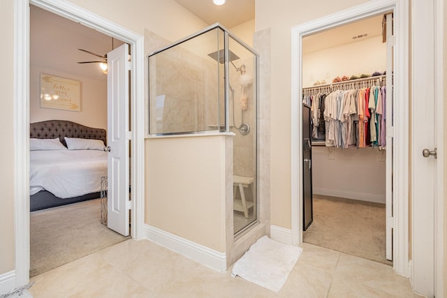 ensuite bathroom with tile patterned floors, ceiling fan, a stall shower, a walk in closet, and baseboards