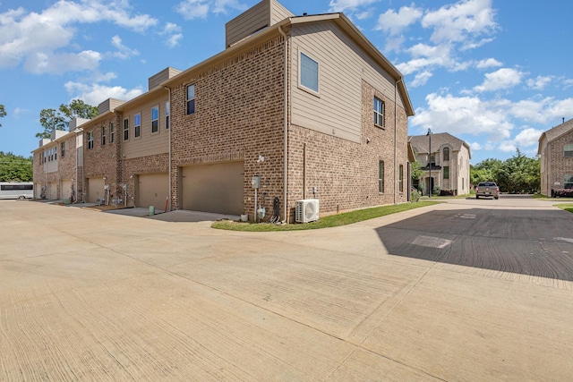 view of home's exterior featuring brick siding, a chimney, ac unit, an attached garage, and driveway