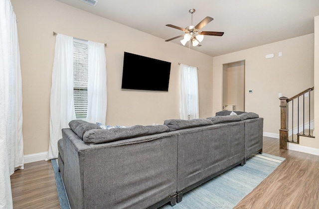 living area with wood finished floors, a ceiling fan, baseboards, and stairs