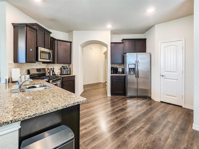601 Bassett Hall Rd, Fate, TX 75189 - kitchen featuring dark brown cabinets, stainless steel appliances, light stone countertops, arched walkways, and backsplash