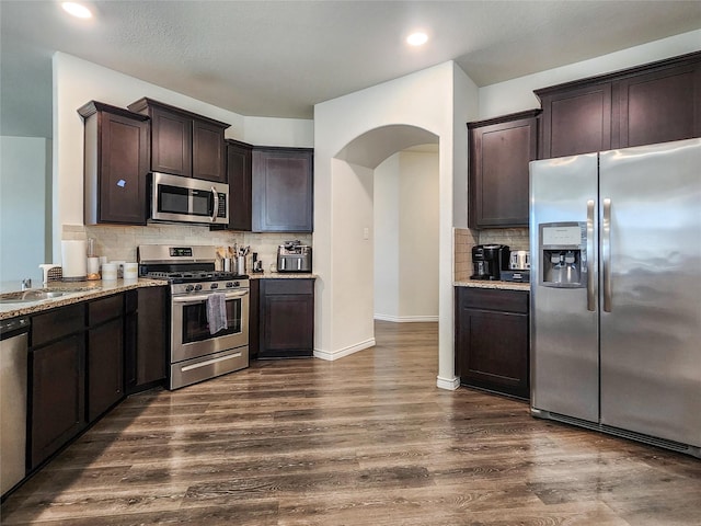 601 Bassett Hall Rd, Fate, TX 75189 - kitchen featuring dark brown cabinets, a sink, light stone countertops, arched walkways, and appliances with stainless steel finishes