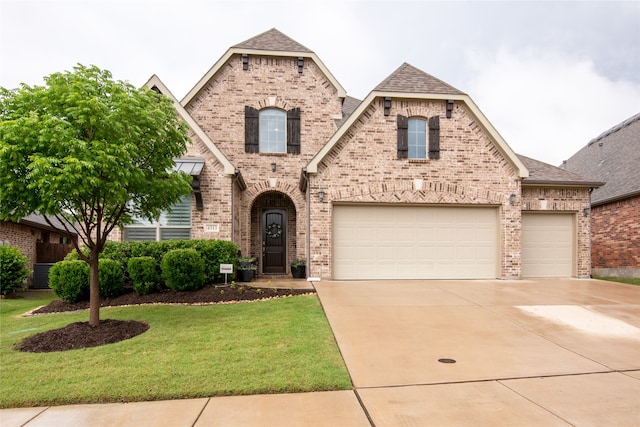 french provincial home with brick siding, concrete driveway, a front yard, and a shingled roof