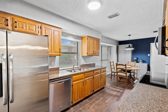 kitchen featuring stainless steel appliances, a sink, dark wood-style flooring, a textured ceiling, and decorative light fixtures