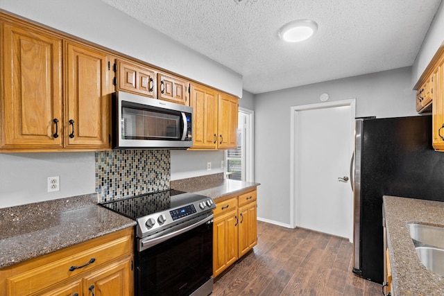 kitchen with appliances with stainless steel finishes, dark wood-style flooring, a textured ceiling, dark stone countertops, and backsplash