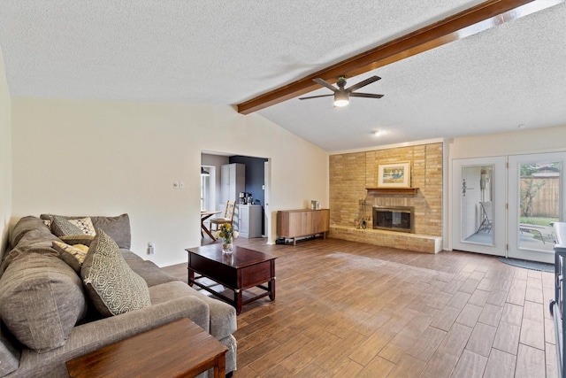 living room with a ceiling fan, a textured ceiling, wood finished floors, and a brick fireplace