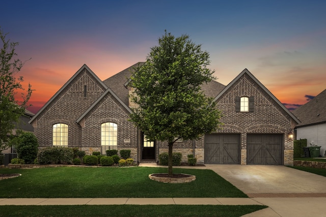 french country inspired facade featuring brick siding, driveway, a front yard, a garage, and stone siding