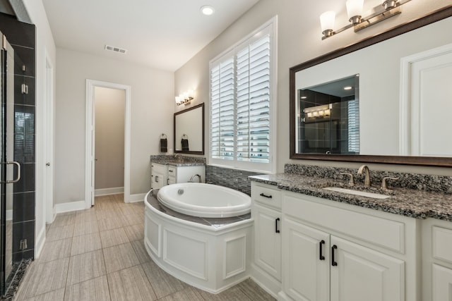 full bath featuring a shower stall, a garden tub, two vanities, and baseboards