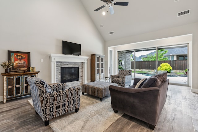living area with high vaulted ceiling, wood finished floors, ceiling fan, a fireplace, and baseboards