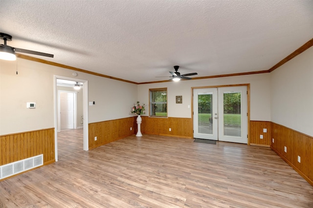 unfurnished room featuring a wainscoted wall, ceiling fan, wood walls, light wood-style flooring, and french doors