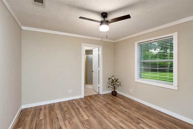 spare room with wood finished floors, a ceiling fan, a textured ceiling, baseboards, and crown molding