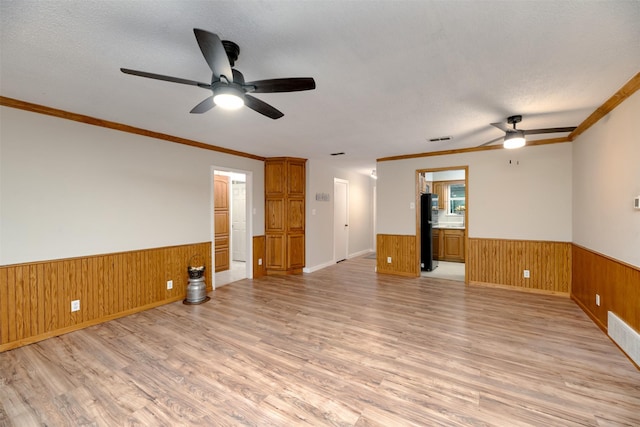 spare room featuring ceiling fan, a wainscoted wall, light wood finished floors, wood walls, and crown molding