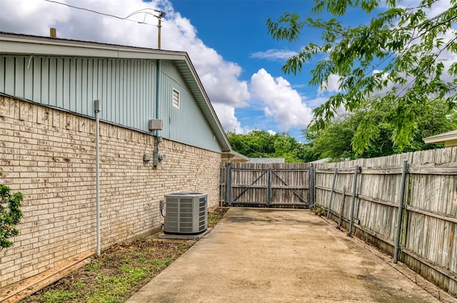 view of property exterior featuring central AC, brick siding, a gate, and fence