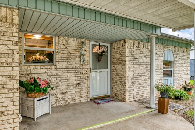 view of exterior entry with brick siding and a porch