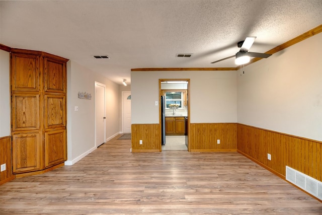 unfurnished room featuring ceiling fan, wainscoting, light wood-style floors, wooden walls, and a textured ceiling