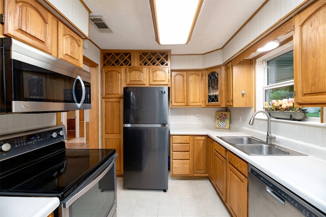 kitchen featuring appliances with stainless steel finishes, a sink, light countertops, glass insert cabinets, and light tile patterned flooring