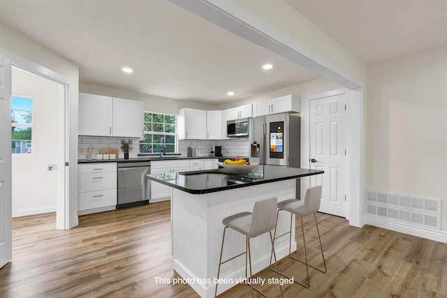 1110 Green St, Abilene, TX 79603 - kitchen with appliances with stainless steel finishes, a kitchen bar, white cabinetry, decorative backsplash, and light wood-style flooring