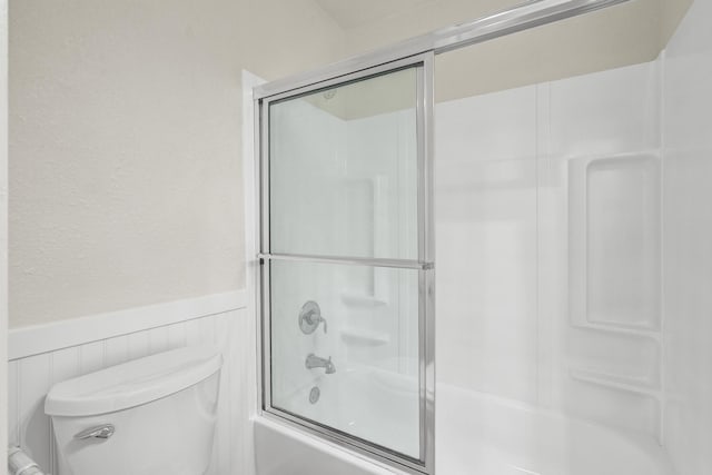 1110 Green St, Abilene, TX 79603 - full bathroom with wainscoting, bath / shower combo with glass door, toilet, and a textured wall