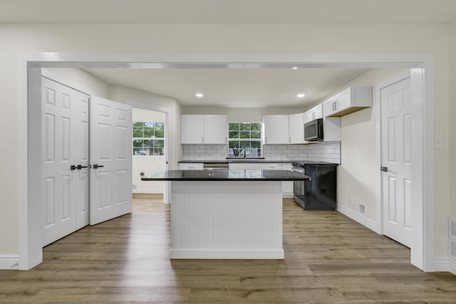 1110 Green St, Abilene, TX 79603 - kitchen featuring range, dark countertops, stainless steel microwave, light wood-style flooring, and white cabinetry