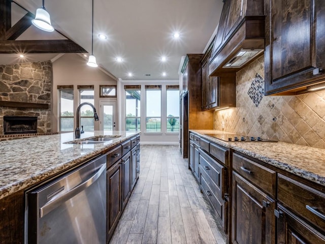kitchen featuring stainless steel dishwasher, a sink, light stone countertops, light wood-style flooring, and backsplash