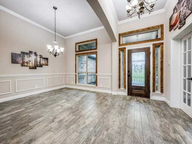 entrance foyer with a chandelier, healthy amount of natural light, ornamental molding, wood finished floors, and a wainscoted wall