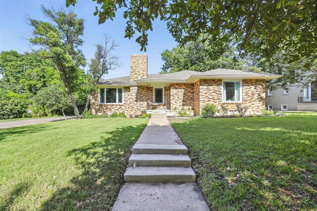 ranch-style home featuring a front lawn, a chimney, and brick siding