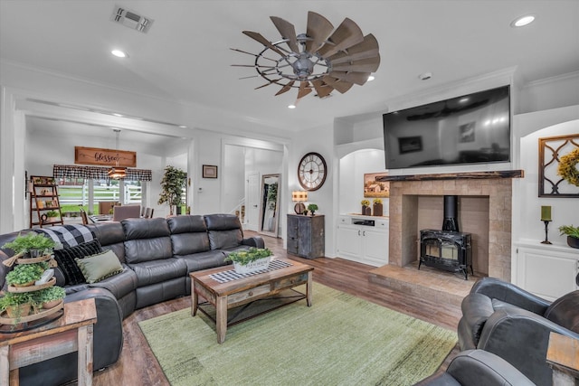 living area with a wood stove, ceiling fan, light wood-style flooring, ornamental molding, and recessed lighting