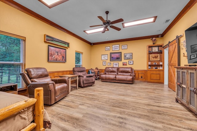 living area featuring ornamental molding, light wood finished floors, a wainscoted wall, a barn door, and a ceiling fan