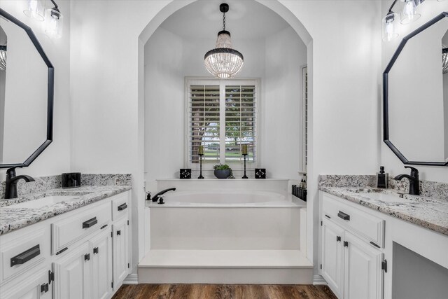 bathroom with a chandelier, wood finished floors, two vanities, and a garden tub