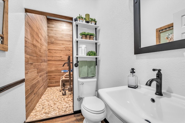 bathroom with a sink, toilet, a textured wall, wood finished floors, and tiled shower