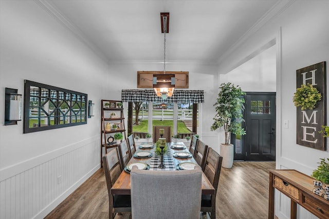 dining area with wood finished floors, crown molding, wainscoting, a chandelier, and a decorative wall
