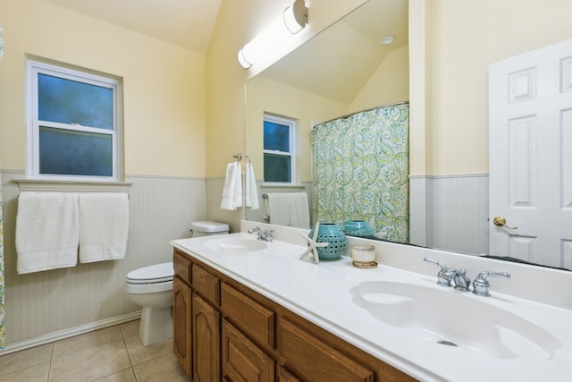 full bathroom with lofted ceiling, toilet, a wainscoted wall, tile patterned flooring, and double vanity