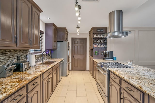 kitchen with stainless steel appliances, a sink, island exhaust hood, backsplash, and light stone countertops